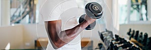 Young African American man standing and lifting a dumbbell with the rack at gym