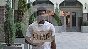 Young African American man stands with a cardboard poster NO RACISM in public outdoor place. An anti racist movement to