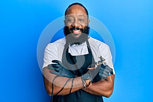 Young african american man tattoo artist wearing professional uniform and gloves holding tattooer machine smiling with a happy and