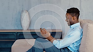 Young african american man texting messages, cheating on his smartphone while sitting on the couch