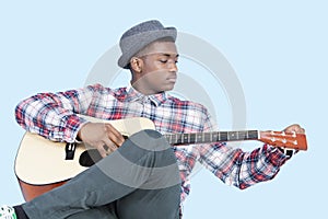 Young African American man tuning guitar over light blue background