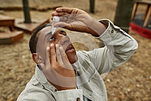 Young african american man using medical eye drops