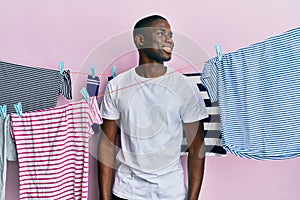 Young african american man washing clothes at clothesline looking to side, relax profile pose with natural face and confident