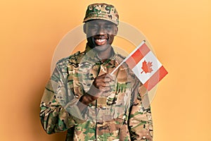 Young african american man wearing army uniform holding canadian flag looking positive and happy standing and smiling with a