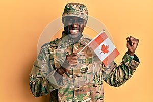 Young african american man wearing army uniform holding canadian flag screaming proud, celebrating victory and success very