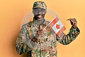 Young african american man wearing army uniform holding canadian flag smiling happy pointing with hand and finger