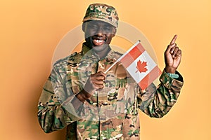 Young african american man wearing army uniform holding canadian flag smiling happy pointing with hand and finger to the side