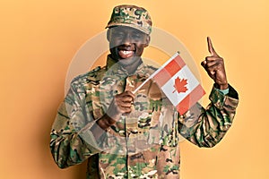 Young african american man wearing army uniform holding canadian flag smiling with an idea or question pointing finger with happy