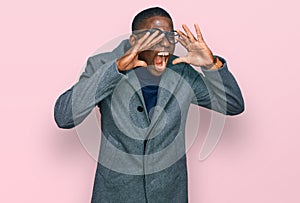 Young african american man wearing business clothes and glasses shouting angry out loud with hands over mouth