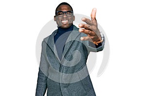 Young african american man wearing business clothes and glasses smiling friendly offering handshake as greeting and welcoming