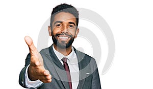Young african american man wearing business clothes smiling friendly offering handshake as greeting and welcoming