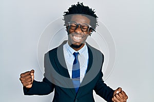 Young african american man wearing business suit very happy and excited doing winner gesture with arms raised, smiling and