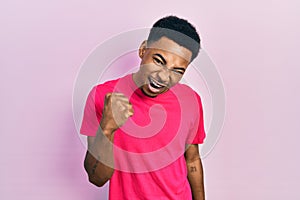 Young african american man wearing casua t shirt angry and mad raising fist frustrated and furious while shouting with anger