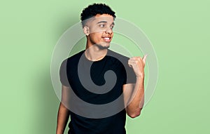 Young african american man wearing casual black t shirt pointing thumb up to the side smiling happy with open mouth