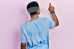 Young african american man wearing casual blue t shirt posing backwards pointing ahead with finger hand