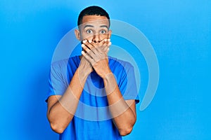 Young african american man wearing casual blue t shirt shocked covering mouth with hands for mistake