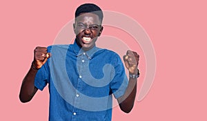 Young african american man wearing casual clothes angry and mad raising fists frustrated and furious while shouting with anger