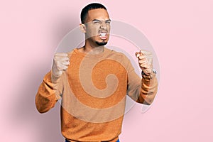 Young african american man wearing casual clothes angry and mad raising fists frustrated and furious while shouting with anger
