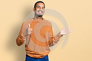 Young african american man wearing casual clothes showing palm hand and doing ok gesture with thumbs up, smiling happy and