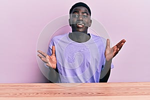 Young african american man wearing casual clothes sitting on the table celebrating victory with happy smile and winner expression