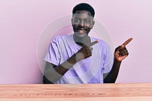Young african american man wearing casual clothes sitting on the table smiling and looking at the camera pointing with two hands