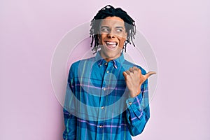 Young african american man wearing casual clothes smiling with happy face looking and pointing to the side with thumb up