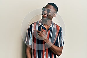 Young african american man wearing casual clothes and sunglasses smiling cheerful pointing with hand and finger up to the side