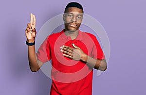 Young african american man wearing casual red t shirt smiling swearing with hand on chest and fingers up, making a loyalty promise