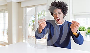 Young african american man wearing casual sweater sitting at home angry and mad raising fists frustrated and furious while