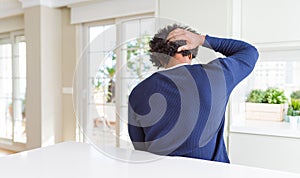 Young african american man wearing casual sweater sitting at home Backwards thinking about doubt with hand on head