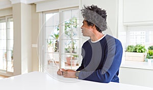 Young african american man wearing casual sweater sitting at home looking to side, relax profile pose with natural face and