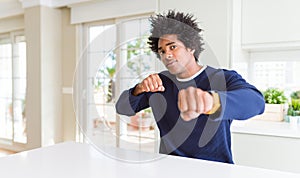 Young african american man wearing casual sweater sitting at home Punching fist to fight, aggressive and angry attack, threat and