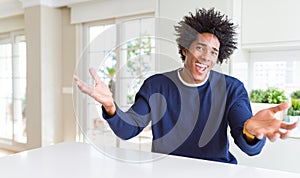 Young african american man wearing casual sweater sitting at home smiling cheerful offering hands giving assistance and acceptance