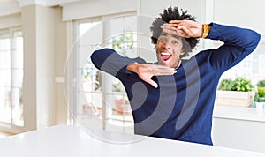 Young african american man wearing casual sweater sitting at home Smiling cheerful playing peek a boo with hands showing face