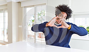 Young african american man wearing casual sweater sitting at home smiling in love doing heart symbol shape with hands