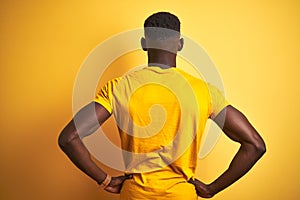 Young african american man wearing casual t-shirt standing over isolated yellow background standing backwards looking away with