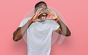 Young african american man wearing casual white t shirt shouting angry out loud with hands over mouth