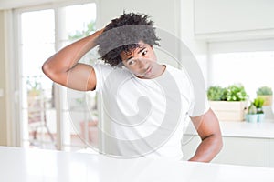 Young african american man wearing casual white t-shirt sitting at home confuse and wondering about question