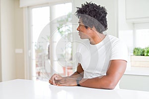 Young african american man wearing casual white t-shirt sitting at home looking to side, relax profile pose with natural face and