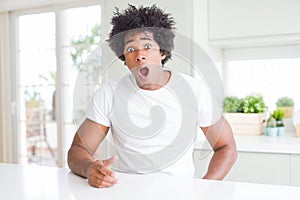Young african american man wearing casual white t-shirt sitting at home In shock face, looking skeptical and sarcastic, surprised
