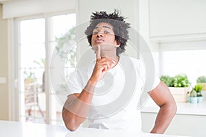 Young african american man wearing casual white t-shirt sitting at home Thinking concentrated about doubt with finger on chin and