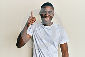 Young african american man wearing casual white t shirt smiling happy and positive, thumb up doing excellent and approval sign