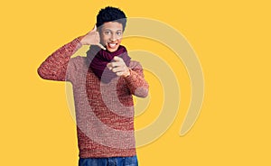 Young african american man wearing casual winter sweater and scarf smiling doing talking on the telephone gesture and pointing to