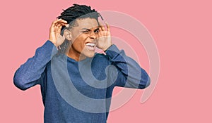 Young african american man wearing casual winter sweater trying to hear both hands on ear gesture, curious for gossip