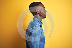 Young african american man wearing denim shirt standing over isolated yellow background looking to side, relax profile pose with