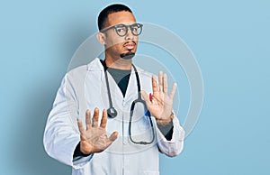 Young african american man wearing doctor uniform and stethoscope moving away hands palms showing refusal and denial with afraid