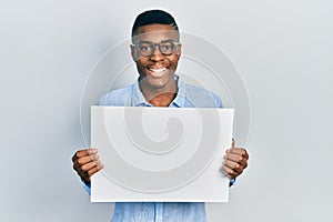 Young african american man wearing glasses holding blank empty banner smiling and laughing hard out loud because funny crazy joke