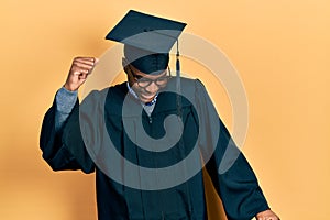 Young african american man wearing graduation cap and ceremony robe dancing happy and cheerful, smiling moving casual and
