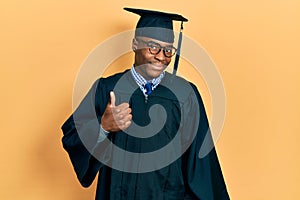 Young african american man wearing graduation cap and ceremony robe doing happy thumbs up gesture with hand