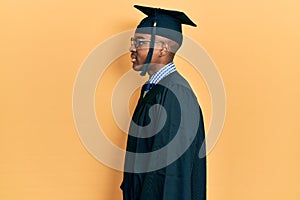 Young african american man wearing graduation cap and ceremony robe looking to side, relax profile pose with natural face and
